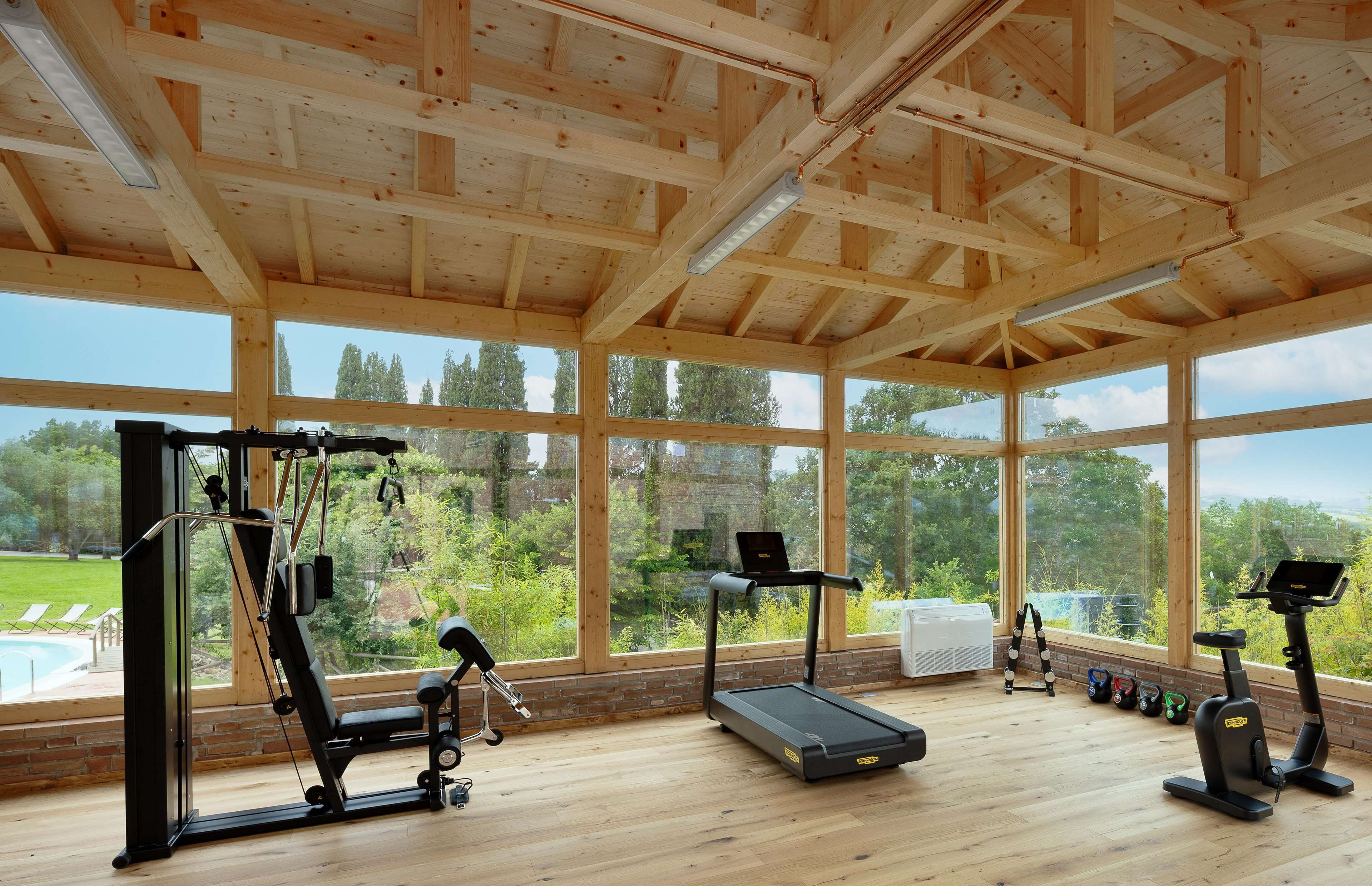 A gym with exercise equipment, large windows, and a view of a swimming pool and greenery.