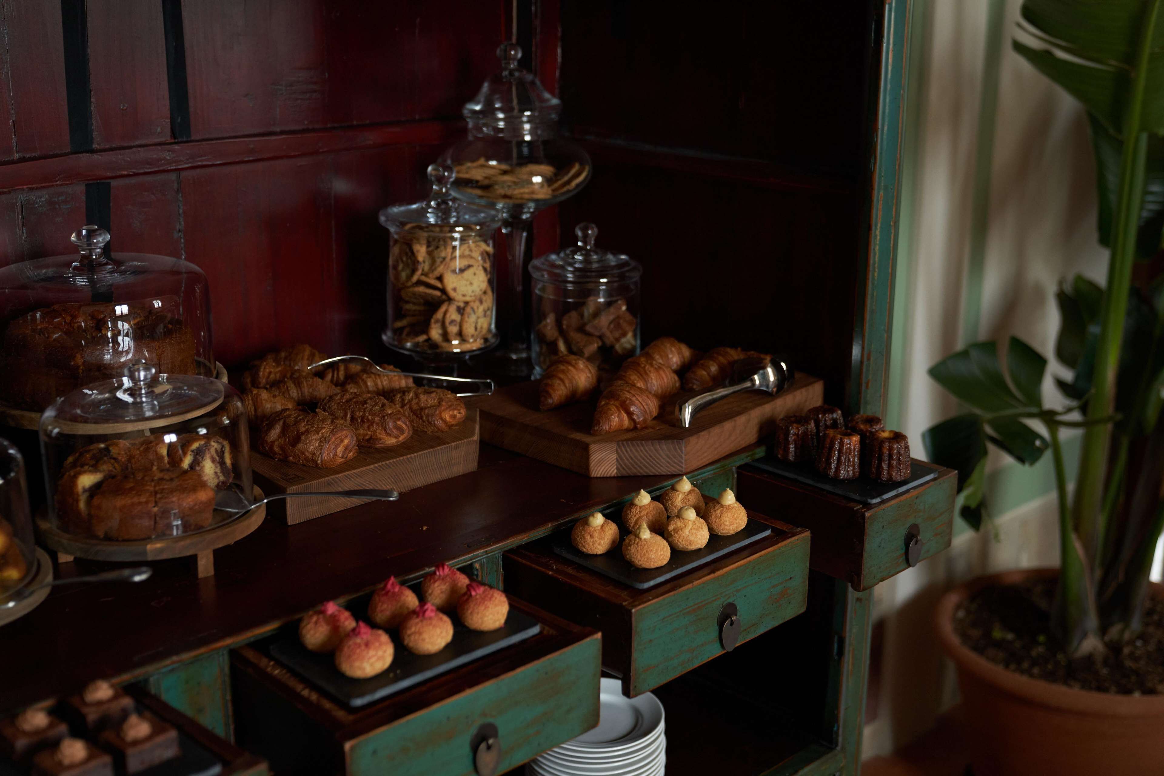 A buffet with various baked goods, including pastries and cookies, displayed on wooden trays and glass containers.