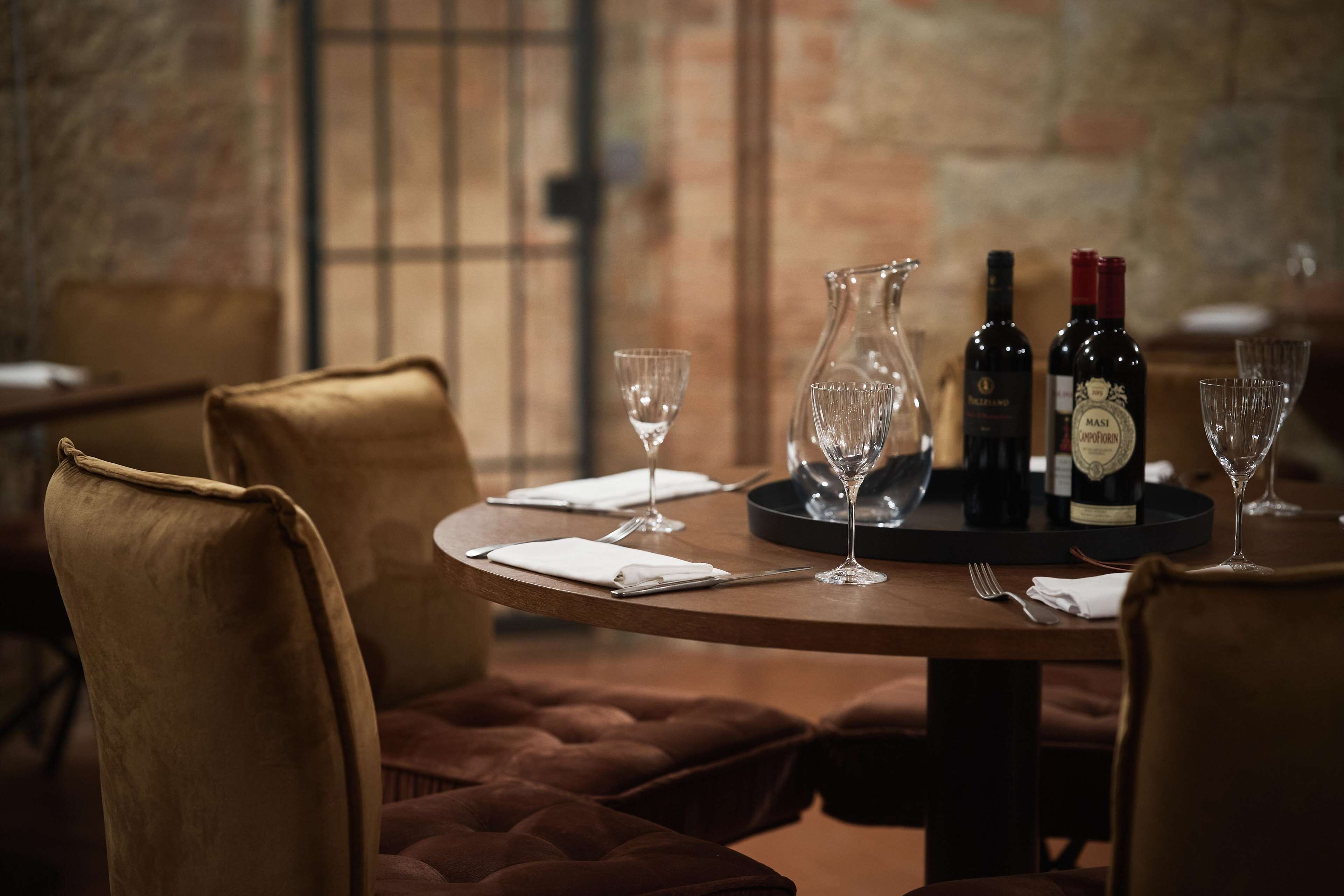Une table à manger dressée avec des bouteilles de vin, des verres et un pichet, entourée de chaises rembourrées.