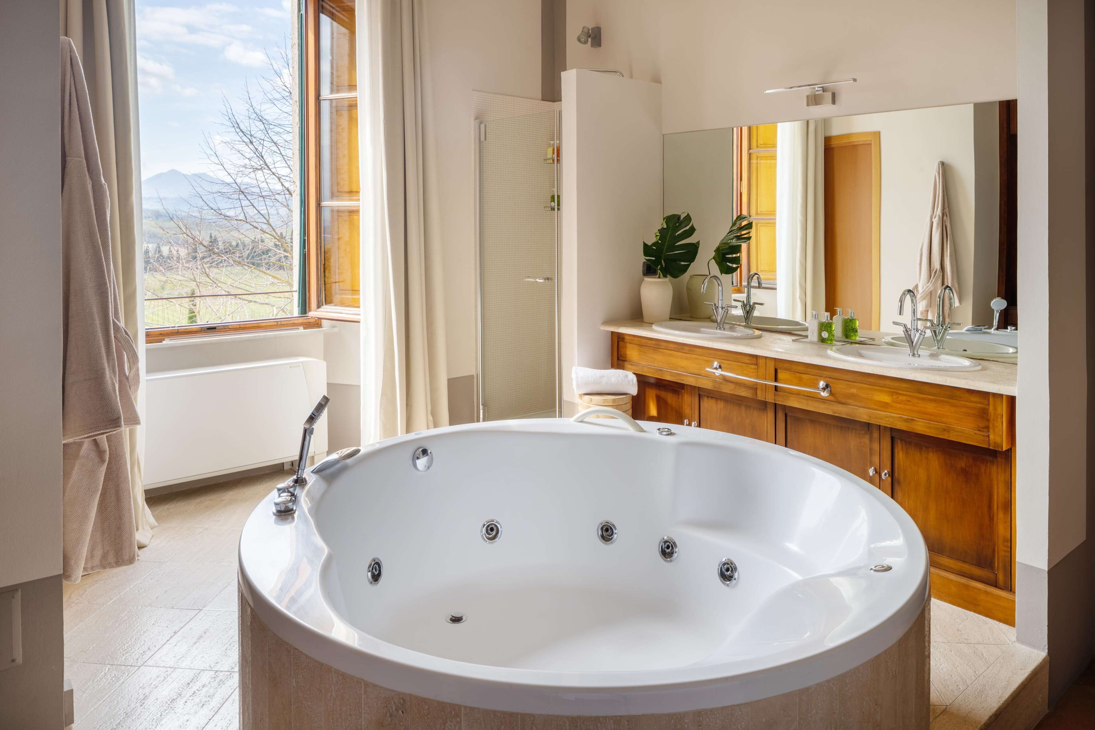 Un bagno moderno con una grande vasca, un mobile contenitore in legno e un ampio specchio.