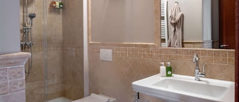 A bathroom with a shower, toilet, bidet, sink, and a towel rack.