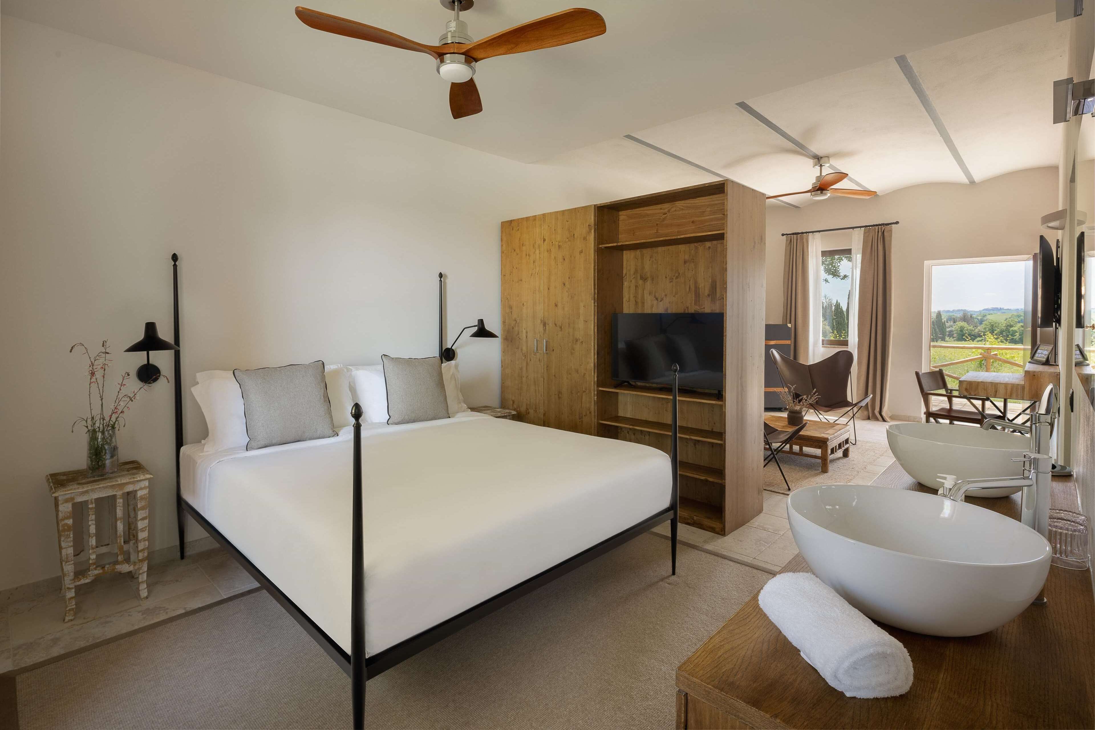 A modern bedroom with a large bed, a wooden wardrobe, a television, a large white bathtub, and a dining area with a view.
