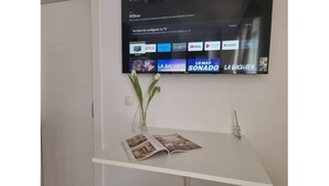 A reception desk with a magazine, a vase with flowers, and a TV displaying streaming services. - 600m de la Playa, Terraza Soleada (Salobreña)