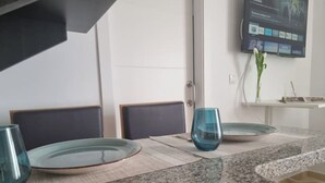 A dining area with a granite countertop, two chairs, a glass table, and a flat-screen TV mounted on the wall. - 600m de la Playa, Terraza Soleada (Salobreña)