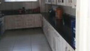 A kitchen with white cabinets, a black countertop, and a window with blinds. - Beachfront Inn (Winterstrand)