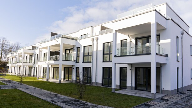 Ein modernes Mehrfamilienhaus mit Balkonen, großen Fenstern und einem gepflegten Rasen.