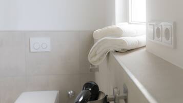 Een badkamer met een wit toilet, een haardroger op een wandhouder, en een raam voor natuurlijk licht.