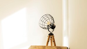 A wooden easel with a wireframe globe sculpture on top, positioned against a plain wall.