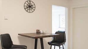 A dining area with a wooden table and two black chairs. A decorative clock is on the wall. - Comfort apartment no. 1 on the first floor on the right (street side, without terrace) (Dormagen)