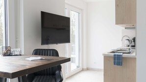A modern kitchen with a flat-screen TV, a dining area with a wooden table and black chairs, and a light-colored floor. - Penthouse apartment no. 10 on the 2nd floor on the right (garden view, large roof terrace) (Dormagen)