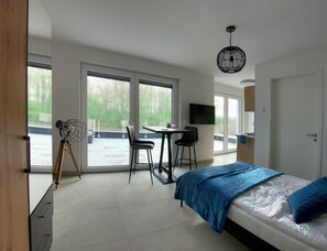 A modern bedroom with a bed, a desk, two chairs, a TV, and large windows. - Penthouse apartment no. 10 on the 2nd floor on the right (garden view, large roof terrace) (Dormagen)