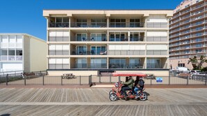 A multi-story hotel with balconies, a wooden boardwalk, and a red vehicle with passengers.