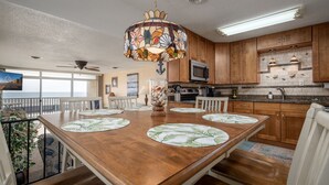 A spacious kitchen with wooden cabinets, a large island with a glass top, and a colorful stained glass pendant light.