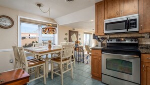 A kitchen with wooden cabinets, a stainless steel oven, a microwave, and a dining area with chairs and a table.