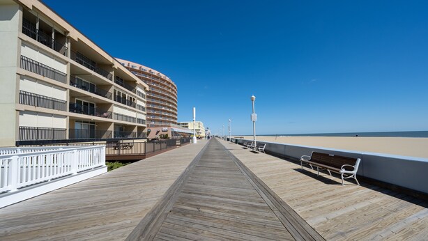 A wooden boardwalk leading to a beachfront hotel with balconies and a beach view.