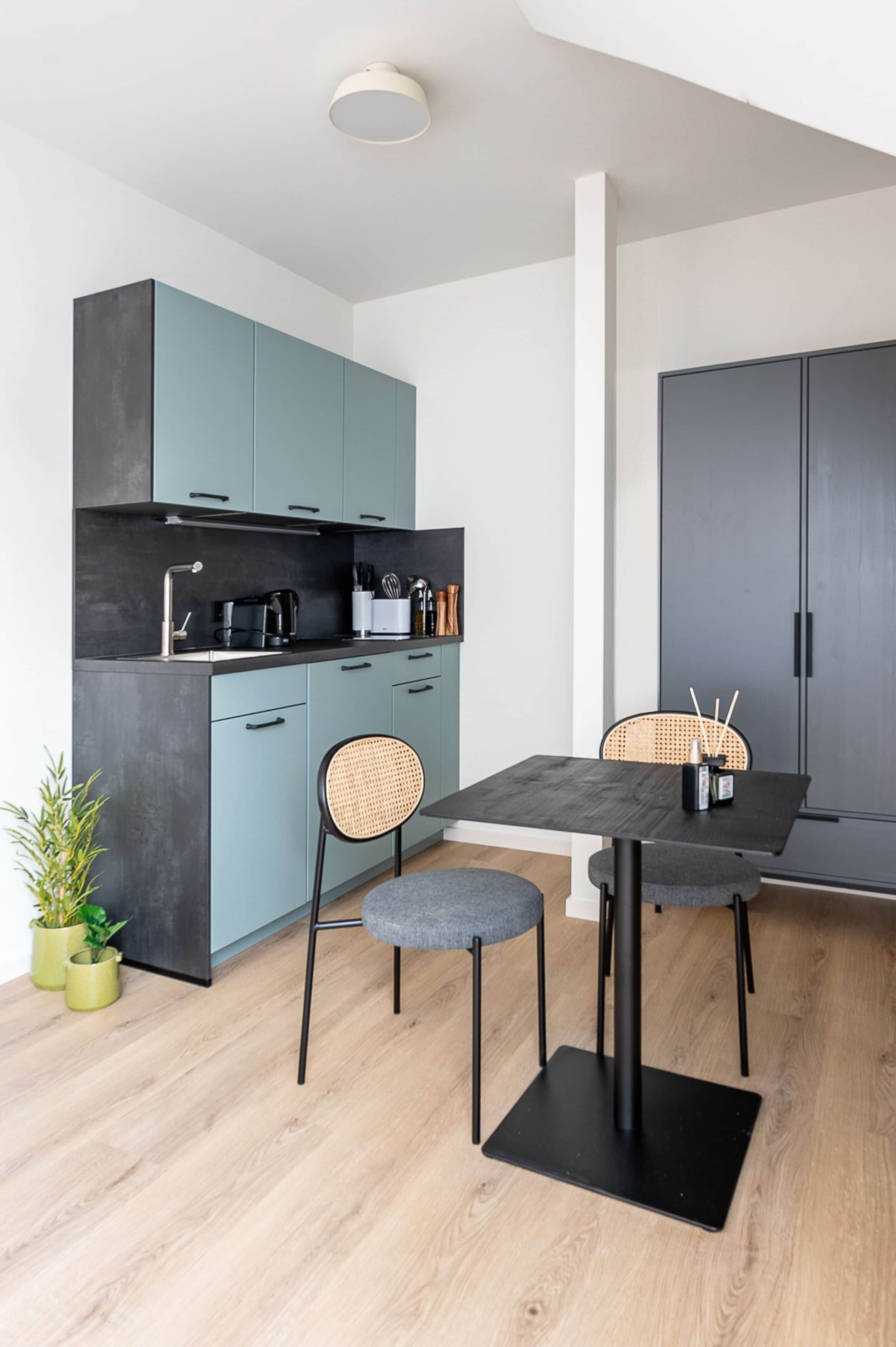 Una cocina moderna con armarios color turquesa, encimera negra y un comedor con dos sillas y una mesa.