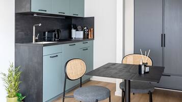 Una cocina moderna con armarios color turquesa, encimera negra y un comedor con dos sillas y una mesa.