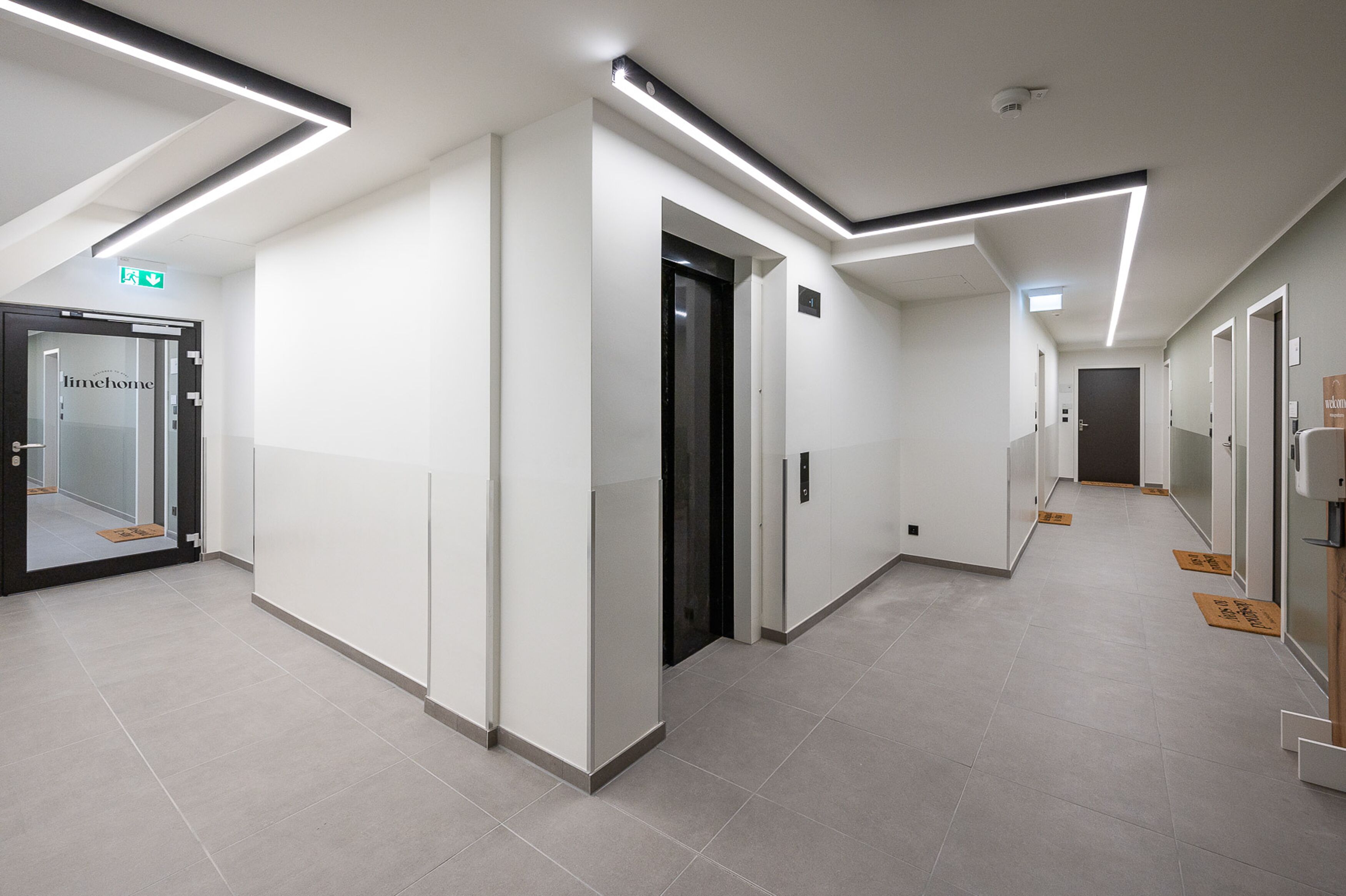 A modern hotel corridor with a glass door labeled "timehome," a black elevator, and a clean, tiled floor.