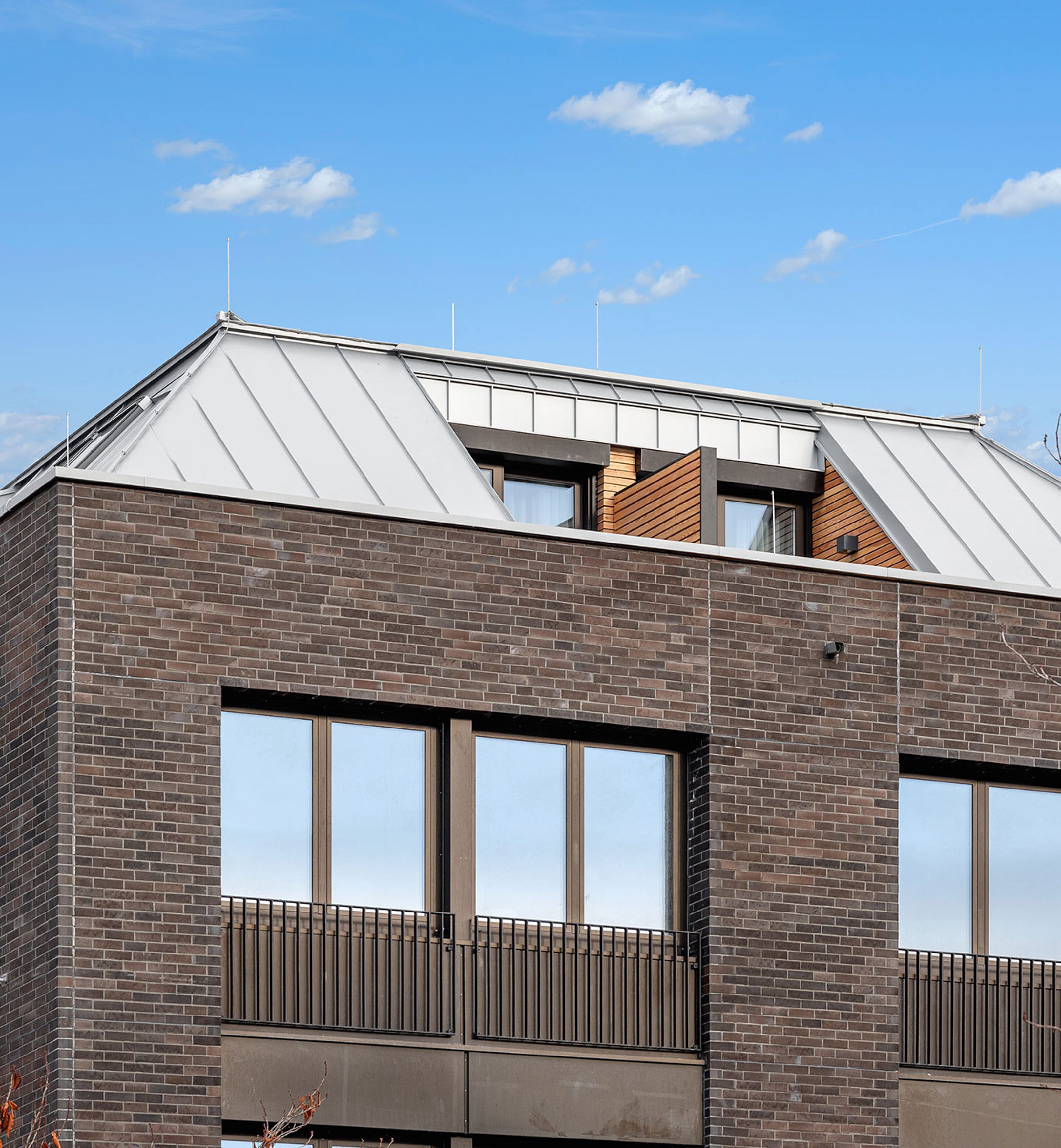 Un bâtiment moderne avec une façade en briques, de grandes fenêtres et un toit métallique incliné.