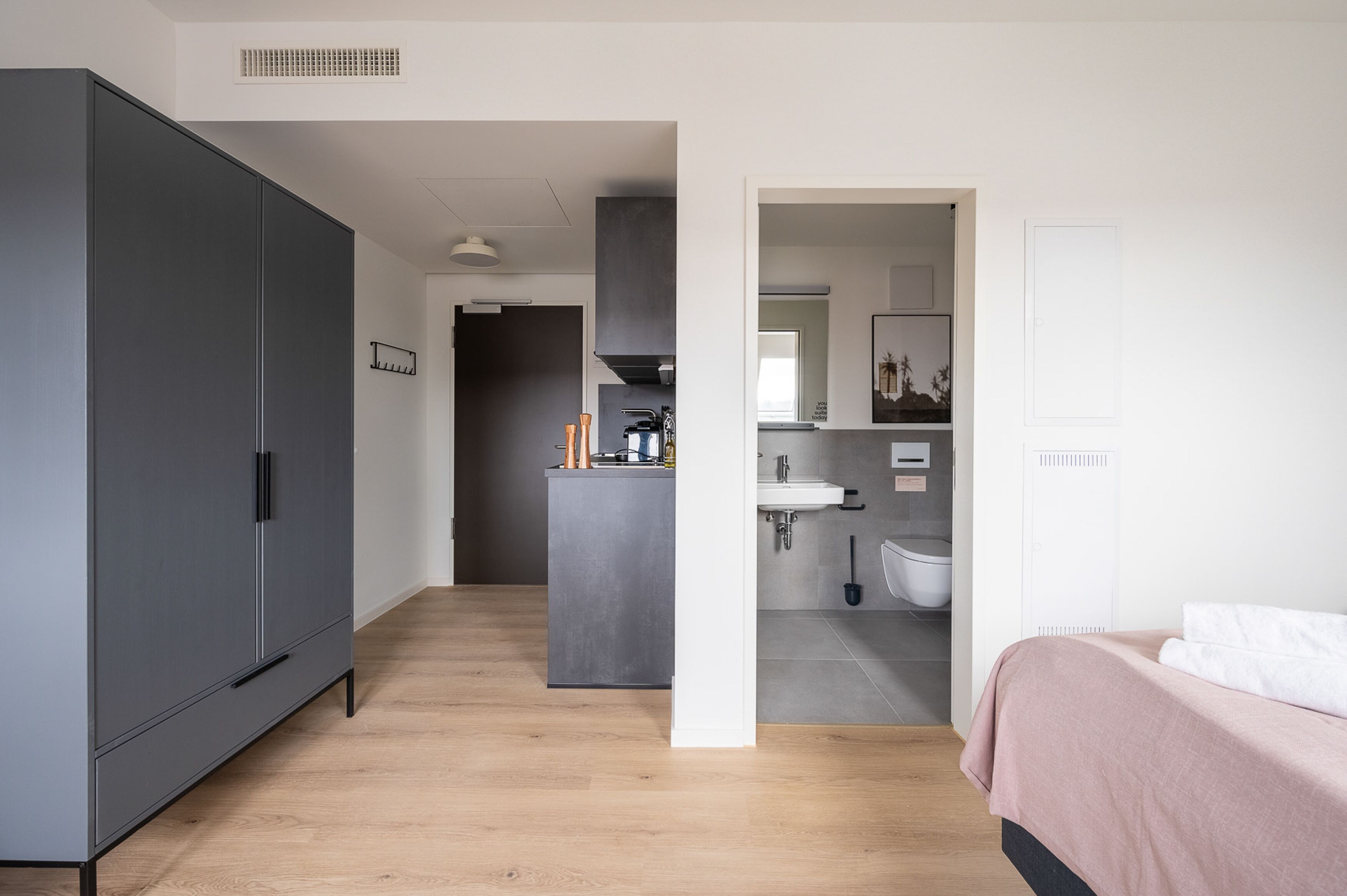 Een moderne slaapkamer met een grote kast, een kleine kitchenette en een badkamer zichtbaar door een open deur.