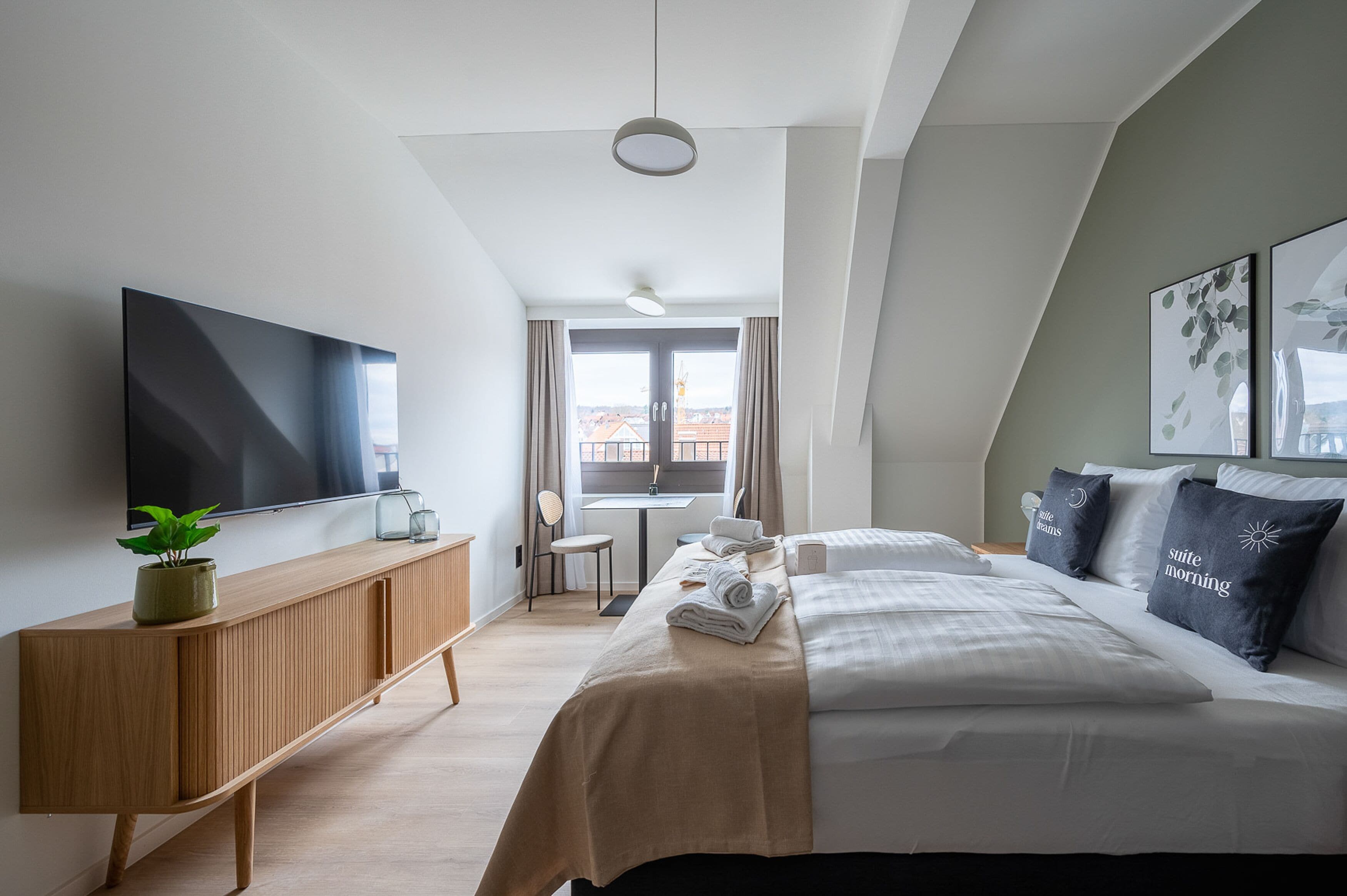 Una camera d'albergo moderna con un grande letto, televisione, un tavolino e vista sulla città.