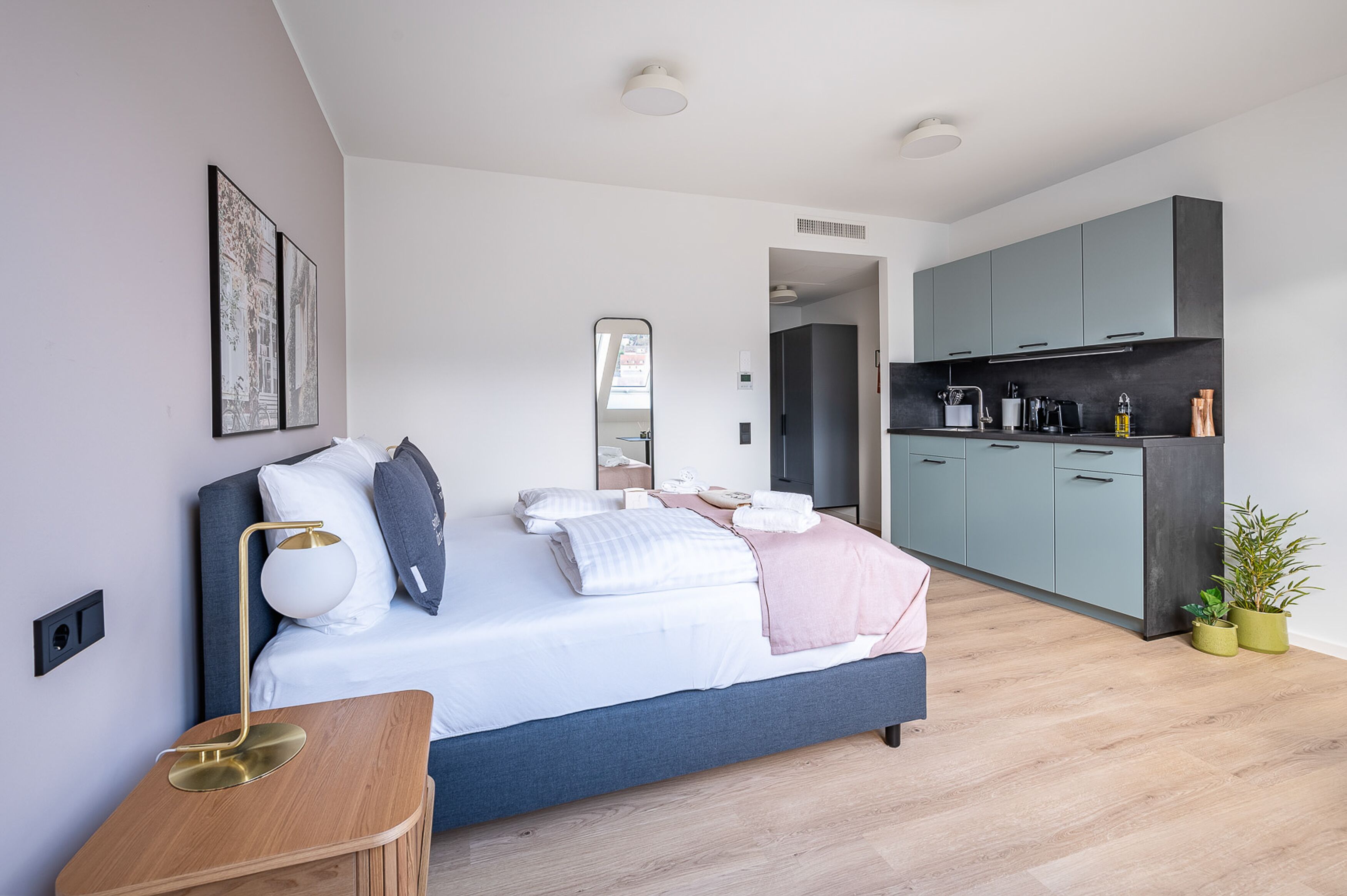 A modern bedroom with a bed, bedside table, and a view into the kitchen.