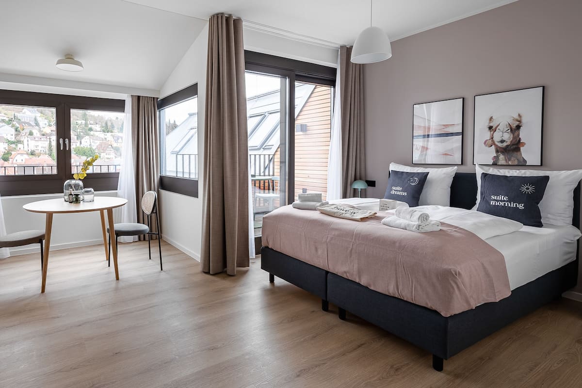 A modern hotel room with a large bed, a round table, and a view of the city.