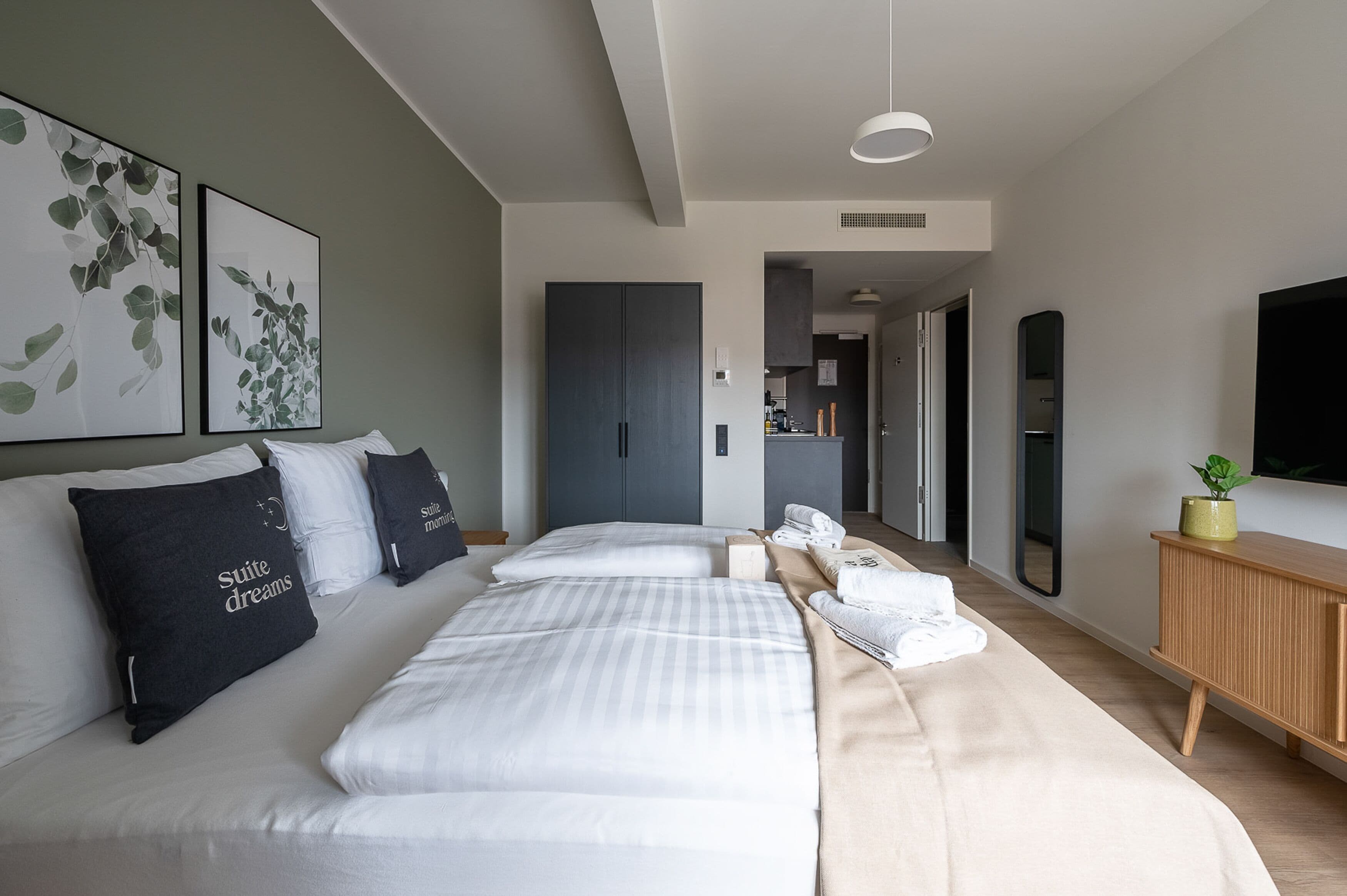 A modern hotel room with a large bed, a wooden console table, and a flat-screen TV mounted on the wall.