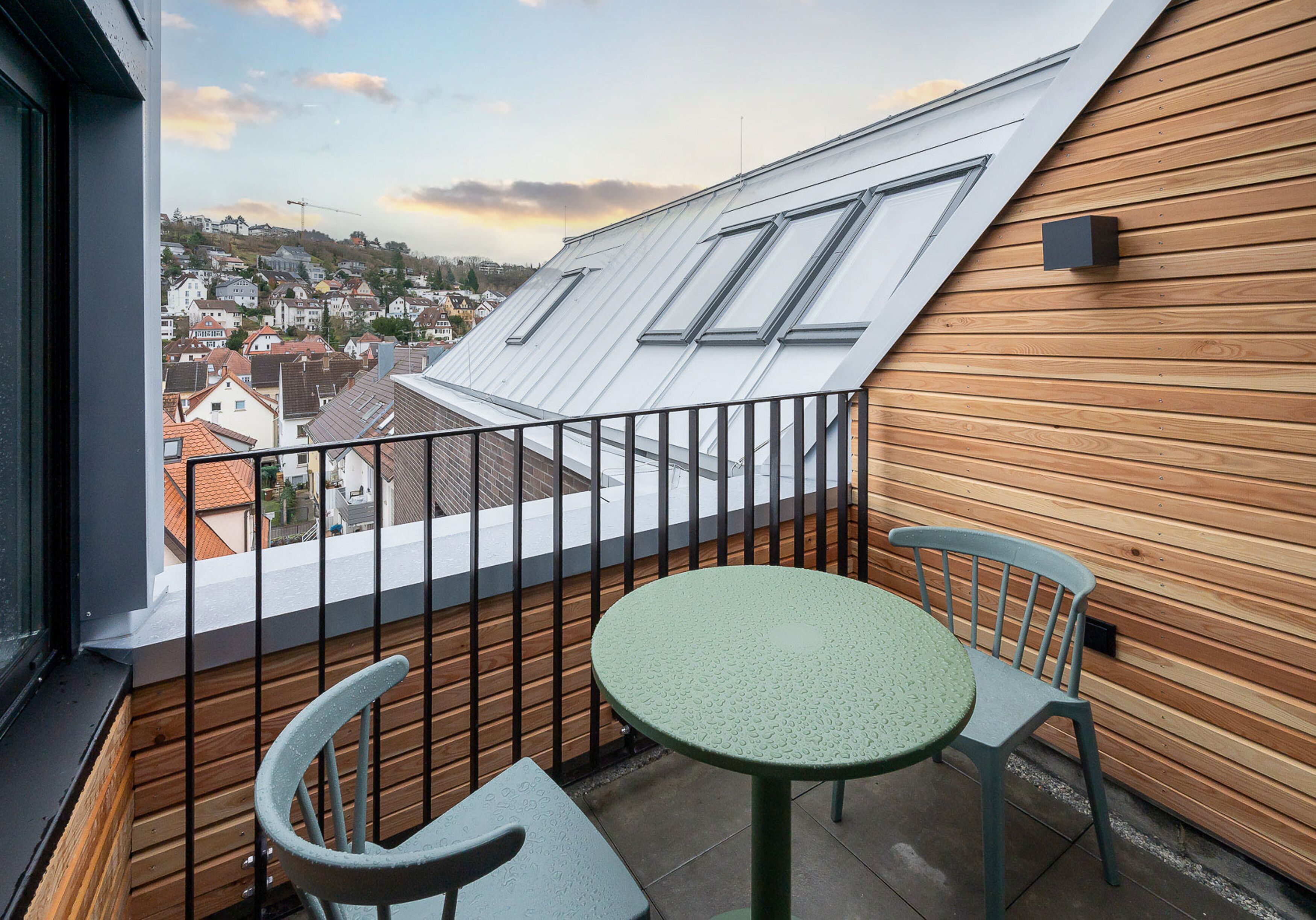 A balcony with a table and chairs, a view of a town, and wooden paneling on the wall.