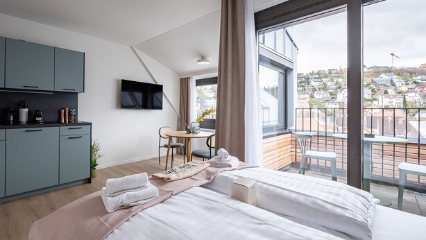 A modern hotel room with two beds, a kitchenette, a dining area, and a balcony with a city view. - Limehome Stuttgart Elsenhansstr. (Stuttgart)