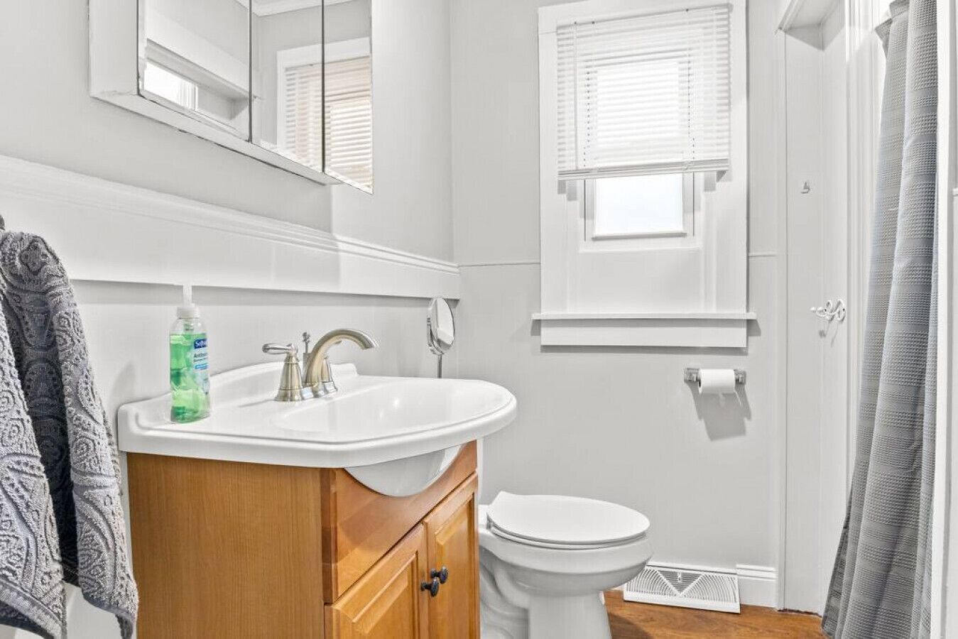 A bathroom with a white sink, mirror, toilet, and window blinds.