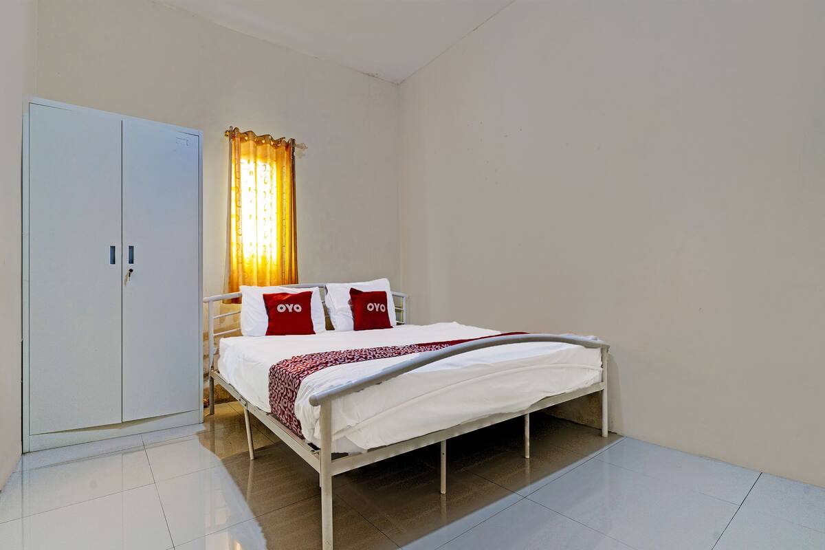 Un dormitorio con cama, cortinas blancas y un armario.
