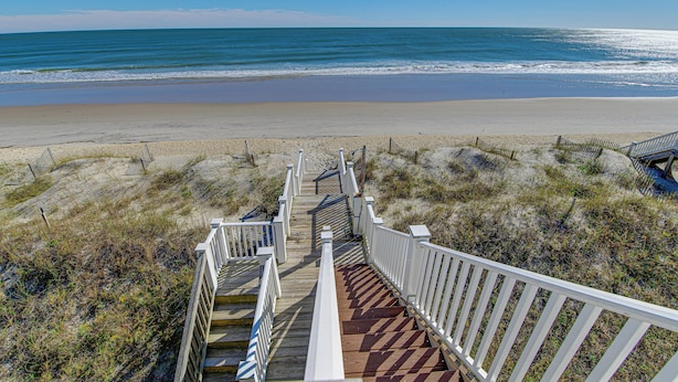 A wooden staircase leading to a beach with a view of the ocean.