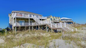 A beachfront property with multiple levels, wooden walkways, and a clear blue sky.