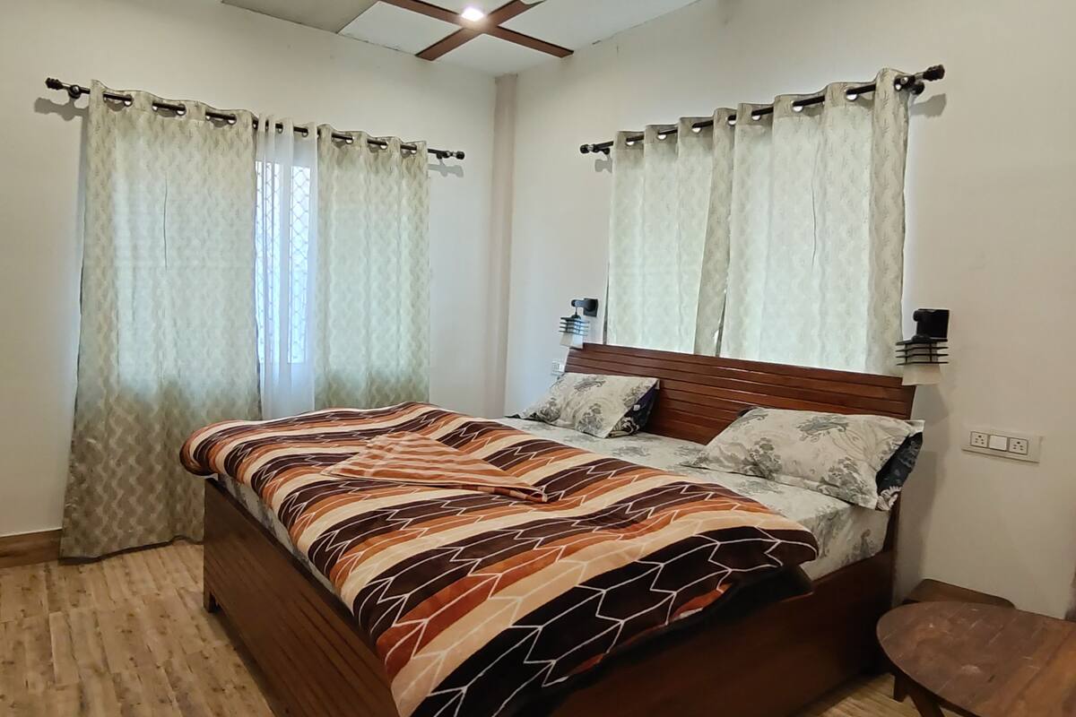 A bedroom with a wooden bed, patterned bedding, a ceiling fan, and curtains.