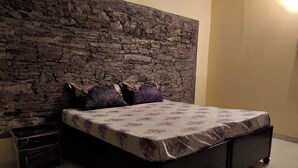A bedroom with a stone wall, a bed with patterned bedding, and a fur rug on the floor. - Atulya Neer Hotel  (Tehri)