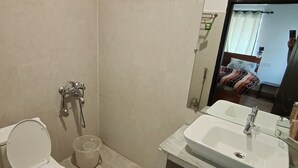 A bathroom with a toilet, bidet, sink, and mirror. - Atulya Neer Hotel  (Tehri)