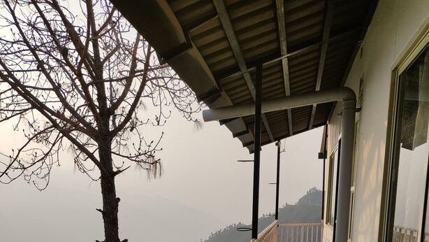 A balcony with a railing, two red chairs, and a view of a mountainous landscape. - Atulya Neer Hotel  (Tehri)