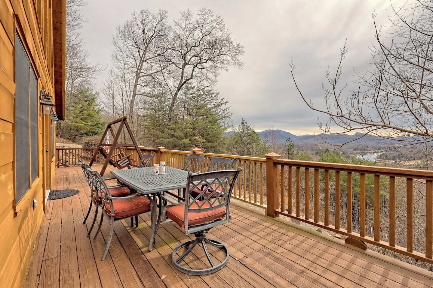 A wooden deck with a table and chairs, overlooking a mountainous landscape.