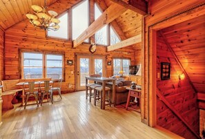 A cozy cabin with a dining area, kitchen, and a large window offering a view. - Hidden Escape Chalet by Chatuge Home Concierge | Lake & Mountain Views · Hot Tub · Firepit (Hayesville)