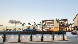Un edificio moderno con fachada de vidrio, zona de estar al aire libre y una pérgola.