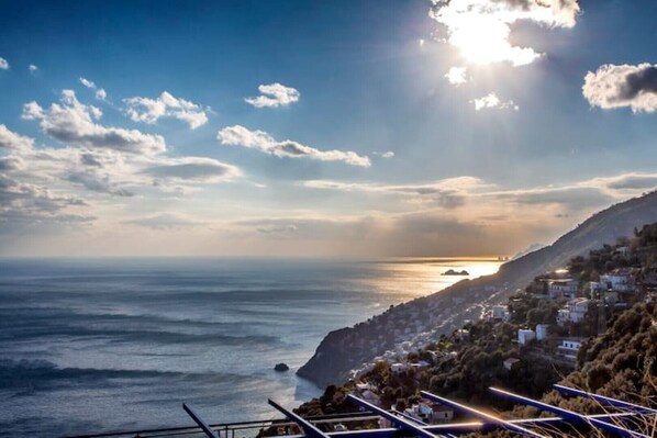 Une vue sur la côte, avec un ciel dégagé, une mer illuminée par le soleil et une colline parsemée de bâtiments.