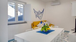A room with a white table, yellow sofa, and a decorative wall hanging. - Domus Teresia - Amalfi Coast (San Michele)