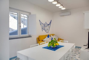 A room with a white table, yellow sofa, and a decorative wall hanging.