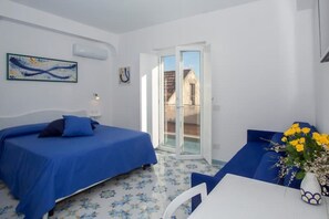 Une chambre d’hôtel avec deux lits, une table et une chaise. Il y a une fenêtre donnant sur les bâtiments environnants.
