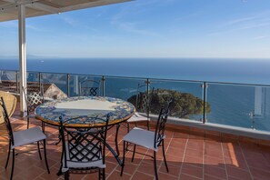 Une terrasse avec une table ronde et des chaises, offrant une vue sur la côte.