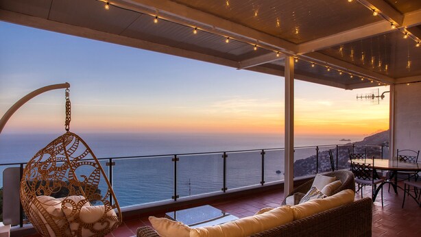 A balcony with wicker furniture, a hanging chair, and a table with chairs, overlooking a scenic ocean view at sunset. - Domus Teresia - Amalfi Coast (San Michele)