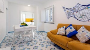 A room with a dining table and chairs, a sofa with patterned cushions, a wall-mounted net decoration, and a window with a view. - Domus Teresia - Amalfi Coast (San Michele)