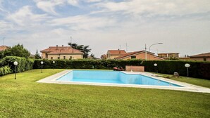 A rectangular swimming pool surrounded by a well-maintained lawn, with houses in the background. - [ZONA POETI] ★★★★★ Relax in Piscina - Free Parking (Loano)