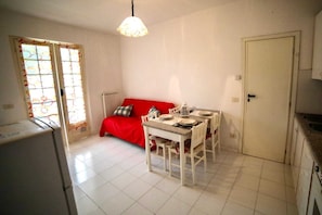 A compact kitchen with a dining table set for four, a red sofa, and a radiator. - [ZONA POETI] ★★★★★ Relax in Piscina - Free Parking (Loano)